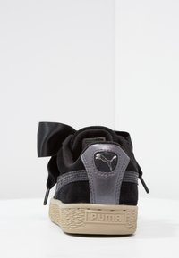 Baskets en daim noir avec une bande texturée grise, des lacets nœud en satin noir et un logo Puma métallique argenté sur le talon. Semelle en caoutchouc gomme.