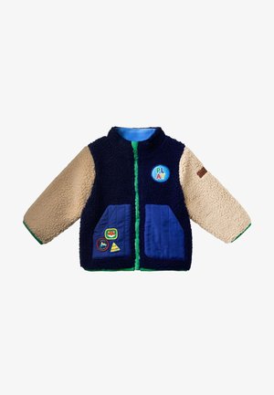 Kinder Reißverschlussjacke mit dunkelblauem Körper, beigen texturierten Ärmeln, blauen Klappentaschen, grünem Besatz und bunten "PLAY"- und Abenteuer-Patches.