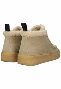 Bottines en daim beige avec doublure en fourrure crème, semelle en caoutchouc et tirants noirs. Présente un design minimaliste avec un branding subtil.
