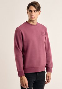 Sudadera burdeos hecha de una mezcla de algodón, con cuello redondo y puños de punto. Incluye un logo circular en el pecho.