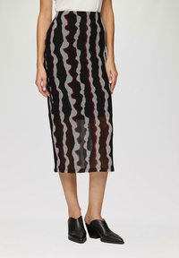 Jupe midi noire, grise et bordeaux avec des motifs ondulés, coupe ajustée et tissu doux et texturé. Associée à des mules noires à talons.