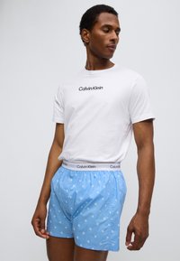 Ανοιχτό μπλε μποξεράκια με λευκό μοτίβο CK, ελαστική μέση με λογότυπο "Calvin Klein"; συνδυασμένα με λευκό T-shirt με στρογγυλή λαιμόκοψη.