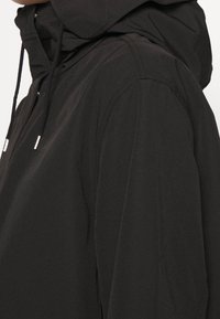 Svart huva jacka med en elegant design, mjuk textur och justerbara dragsnören för passform. Den har kontrasterande sömmar.