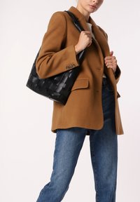 Zwarte geweven leren handtas met een gladde afwerking, met een gestructureerd tote-ontwerp. Draagt met een bruine jas en blauwe jeans.