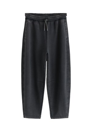 Nahaufnahme einer Person, die schwarze Sweatpants mit elastischem Bund und Kordelzug trägt, mit der Hand in der linken Tasche.
