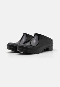 Black clogs made of shiny material with a smooth upper, textured rubber sole, and open back design for easy wear. Features a chunky profile.