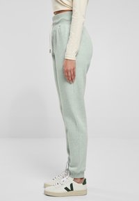 Ljusgröna joggingsbyxor med hög midja, snörning och avsmalnande muddar, tillverkade av mjukt tyg. Matchas med vita sneakers med gröna accenter.