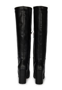 Botas de cuero negras hasta la rodilla con una textura suave, que presentan un tacón grueso y un detalle de cremallera en el costado. Costuras verticales para dar forma.