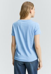 Una camiseta de algodón azul claro con mangas cortas, un escote redondeado y un corte relajado, combinada con unos pantalones vaqueros de denim azul oscuro.