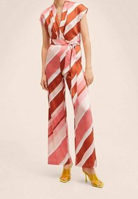 Roze en roest gestreepte jumpsuit met een wikkelvoorkant, korte mouwen, een ceintuur in de taille en brede broekspijpen; gecombineerd met gele hakken.