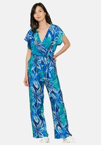 Mėlynas ir žalias gėlių kombinezonas su trumpomis rankovėmis, giliu V formos kaklu, elastingu liemeniu, plačiomis kojomis ir surišamu dirželiu. Minkštas audinio tekstūros.