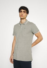 Lys grå polo-skjorte med teksturert stoff, kontrasterende hvit krage og ermebeskyttere, enkel knapplukking og brodert logo på brystet.