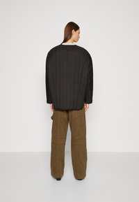 Svart quilted oversized jakke med ribbet tekstur og sømdetaljer, brukt over olivengrønne vide cargo-bukser.
