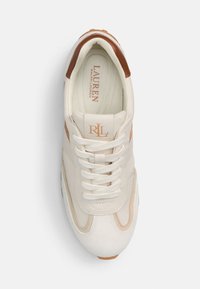Jasno beżowe sneakersy z teksturowanym zamszowym noskiem i brązowymi akcentami. Posiadają białe sznurowadła oraz wyraźne logo na języku i pięcie.