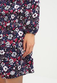 Blommig klänning i mörkblått med rosa, vit och svarta mönster. Har långa ärmar, elastisk midja och lätt tyg.