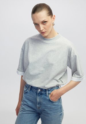 T-shirt en coton gris avec une coupe décontractée, présentant des manches roulées et un col rond, associé à un jean en denim bleu clair.