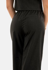 Tuta nera in tessuto a coste con un corpetto aderente e vita elastica, caratterizzata da un design minimalista e tasche laterali.