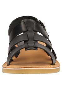Sandale en cuir noir avec plusieurs lanières et boucle latérale, semelle beige avec couture visible, vue de face.