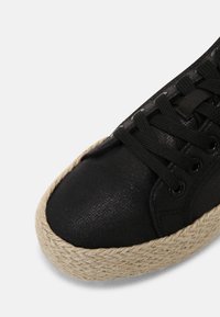 Černá teniska s texturovaným svrškem, střední podrážkou z proplétaného juty a gumovou podrážkou. Šněrovadla jsou černá s kulatými průvleky pro zapínání.