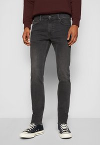 Dunkelgraue Denim-Jeans im Slim-Fit-Design, mit subtilen Ausbleichungen und einem klassischen Fünf-Taschen-Stil, kombiniert mit schwarzen Sneakers.