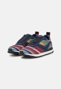 Sneakers sportivi con una tomaia in mesh caratterizzata da strisce orizzontali multicolori, accenti blu navy e una suola nera testurizzata. Dettaglio del tab per il tallone rosso.