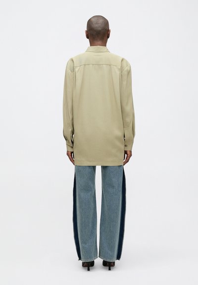 Šviesiai béžinė ilgomis rankovėmis marškinėliai su apykakle, derinami su mėlynomis plačiomis džinsomis, turinčiomis tamsias šonines juostas ir neišbaigtu kraštu, vilkima su juodais aukštakulniais.