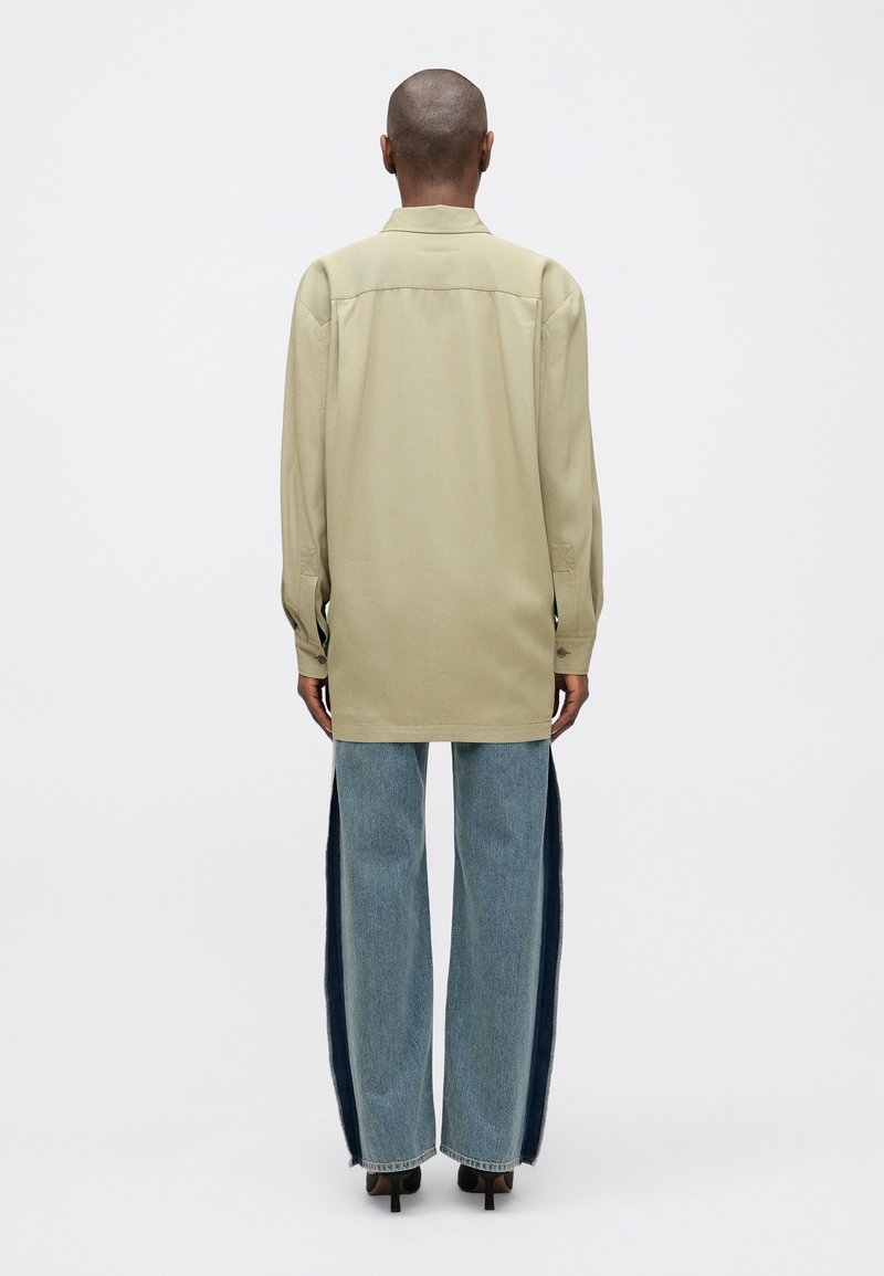 Ljusbeige långärmad skjorta med krage, parat med blå vida jeans med mörka sidopaneler och råa kantar, bärs med svarta klackar.