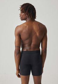 Zwarte katoenen boxershorts met een gladde tailleband, een aansluitend ontwerp en naadloze constructie, weergegeven op een persoon die van achteren te zien is.