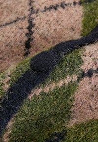 Vilnas audums ar rūtainu rakstu, kas iekļauj zaļu, rozā un melnu krāsu. Tekstūra ir mīksta un pūkaina, ar redzamām šķiedrām.