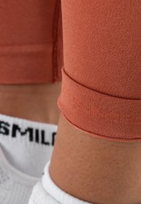 Světle oranžové sportovní legíny s přiléhavým designem, se zahnutým lemem. Bílé ponožky s černým textem "SMILE" jsou viditelné.