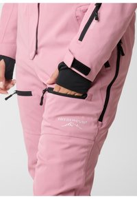 Pink outerwear with a smooth texture, featuring black zippers, Velcro cuffs, and a logo on the thigh. Multiple zippered pockets are visible.