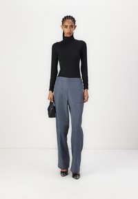 Schwarzes Rollkragen-Shirt und hellgraue, weit geschnittene Hose mit Fronttaschen und glatter Textur. Eine schwarze Handtasche und glänzende Schuhe runden den Look ab.