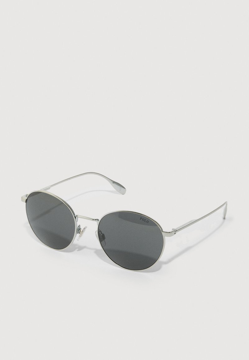 Óculos de sol redondos com lentes escuras e uma estrutura fina de metal prateado. As hastes apresentam detalhes transparentes. O nome da marca "POLO" está visível no canto superior esquerdo da lente.