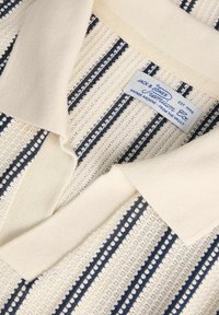 Polo en tricot blanc cassé avec rayures bleu marine. Col côtelé et tissu texturé avec de petites découpes. L'étiquette indique "Jack & Jones Premium."