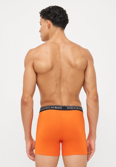 Oranžne bombažne bokserice z črnim pasom, na katerem je napis "Polo Ralph Lauren". Gladka tekstura, prilegajoča se zasnova in dolžina do sredine stegna.
