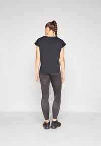Black short-sleeve top, paired with dark grey leggings featuring a striped accent. Model stands with back facing, wearing black shoes.