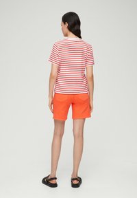 Rood-wit gestreepte korte mouwen t-shirt in combinatie met oranje shorts. De shorts hebben twee achterzakken. Draagt het met zwarte sliders.