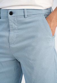 Ljust blå byxor i texturerad väv med ett subtilt mönster, sidfickor, knappstängning och bälteshällor.