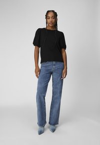 Blouse noire à manches courtes avec manches bouffantes, associée à un jean droit bleu et des escarpins bleu clair à bout pointu.