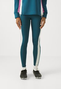 Leggings bleu sarcelle avec des bandes blanches sur les côtés, associés à un haut bleu agrémenté de touches roses. Le tissu a une texture lisse, adaptée au sport.
