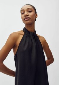 Mustat halterneck-topit, joissa on kerätty pääntie, ja joissa on virtaava, kevyt kangas, joka laskeutuu elegantisti olkapäiden ja käsivarsien ympärille.