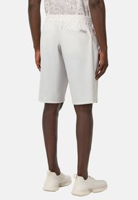 Shorts de sport blancs avec une taille élastique, deux poches latérales et une poche arrière. Texture lisse, coupe au genou, design minimaliste.