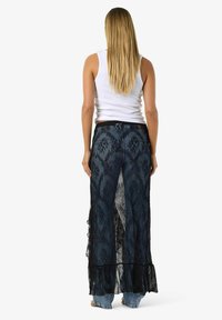 Krajková maxi sukně tmavě modré barvy s propracovanými vzory, vrstveným designem a volánkovým lemem. Kombinováno s světlými džínami a bílým tílkem.