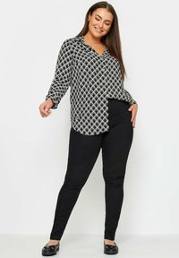 Czarna i biała bluzka z falistym wzorem, długimi rękawami i kołnierzykiem, połączona z czarnymi obcisłymi dżinsami i czarnymi balerinami.
