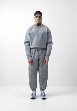 Grå teksturert hettegenser og matchende joggebukser med elastiske mansjetter. Utstyrt med strikk i livet og parret med hvit-blå sneakers.