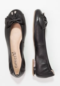 Une paire de ballerines noires en cuir avec des orteils ronds, des nœuds décoratifs avec des embouts métalliques, des semelles intérieures beiges et de petits talons métalliques.