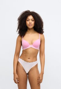 Różowy stanik z koronkowym wykończeniem, z wypełnionymi miseczkami i regulowanymi ramiączkami, w zestawie z przezroczystymi białymi stringami z koronkowym pasem.