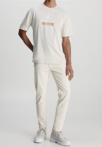 Camiseta de manga corta de color crema claro con el logo "Calvin Klein Jeans", combinada con pantalones ajustados de color crema claro y zapatillas altas beige.