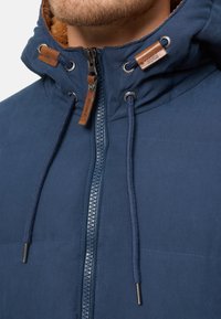Veste bleu marine avec une fermeture éclair à l'avant, une capuche et des cordons de serrage. Présente des accents en cuir et une doublure intérieure douce pour plus de chaleur.