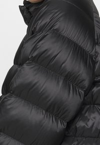 Sort puffer jakke med kviltede sektioner, skinnende tekstur, høj krave og en strømlinet silhuet. Velegnet til koldt vejr.
